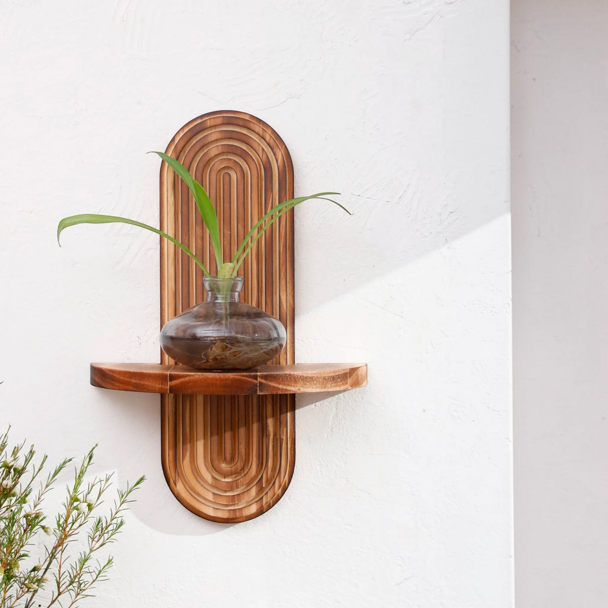 Étagère murale en bois Royaume de L'Étagère avec motif strié arrondi et vase en verre sur fond blanc texturé
