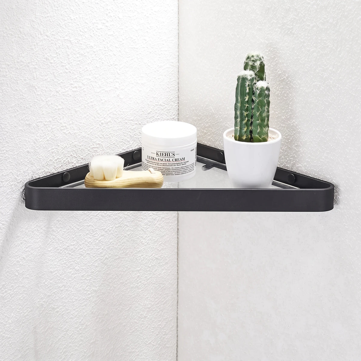 Étagère murale d'angle noire Royaume de L'Étagère avec produits de soin et cactus sur un mur blanc texturé